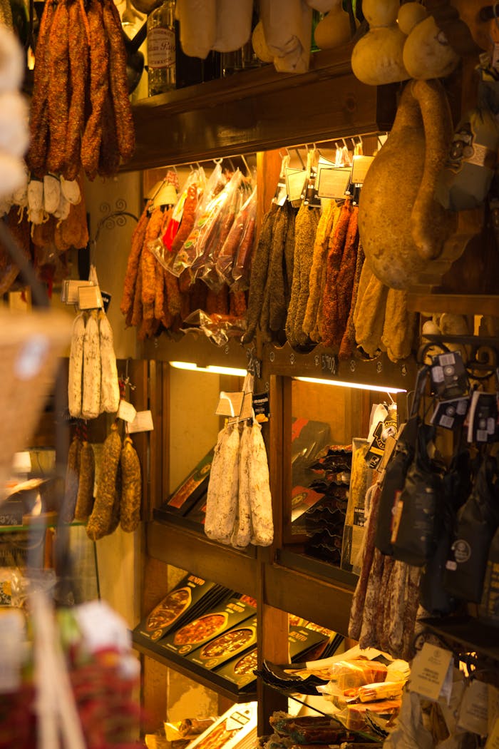 gallery-05 Cured meats hanging on shelves in a rustic gourmet food shop, warm ambiance.